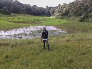 Alfred Mepukori standing near Ilturot natural water catchment area in Naimina Enkiyio Forest